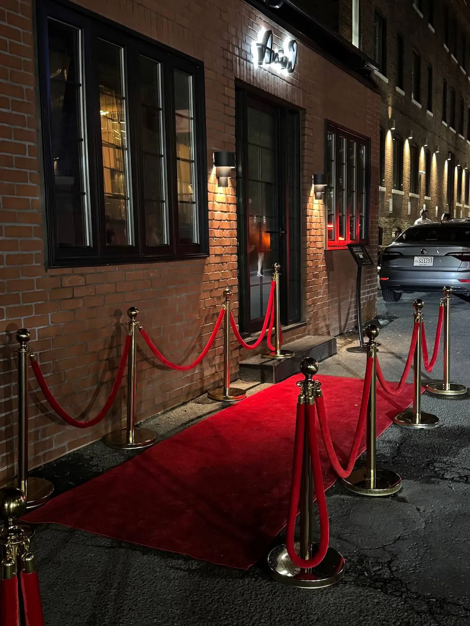 Gold rope stanchions with red velvet ropes beside a red carpet at an evening entrance